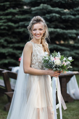 Fototapeta na wymiar Attractive bride posing with bridal nosegay on open air looking at camera