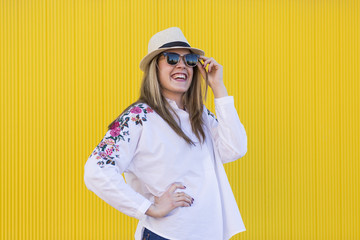 beautiful young woman holding sunglasses and smiling. Yellow background. Lifestyle