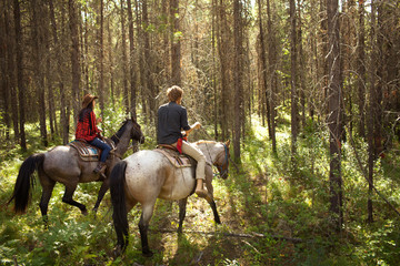 Man and woman riding horses through woods