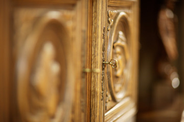The brass key in the door of an antique carved wooden cabinet.