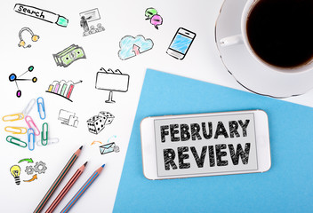 February Review. Mobile phone and coffee cup on a white office desk.
