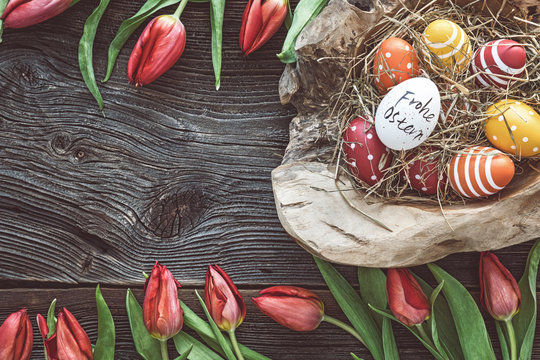 Frohes Osternest mit roten Tulpen auf rustikalem Holzbrett
