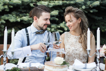 Groom and bride drinking champagne on a table in a decorative autumn forest, happy newlyweds