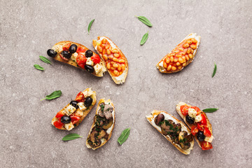 Variety of small bruschetta with caprese salad , white beans on the grill with tomato sauce and fried mushrooms with soft cheese, served on grey  background.