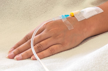 Patient's hand with medicine drip injection, lady on a bed in a hospital