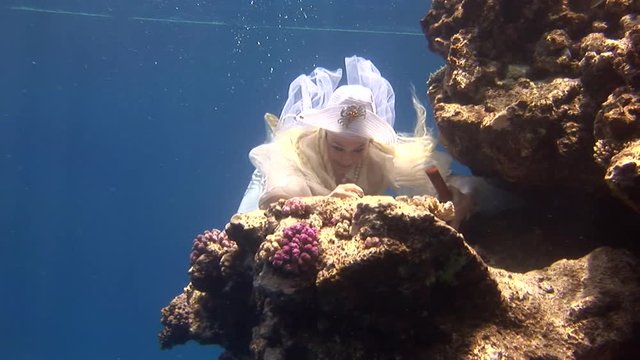 Underwater model free diver in costume pirate swims in clean water in Red Sea. Filming a movie. Young girl smiling at camera. Extreme sport in marine landscape, coral reefs, ocean inhabitants.