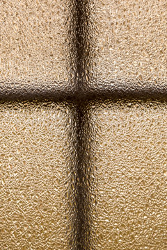 Closeup of frosted bronze like window glass with a cross shape and sharp shiny abstract texture. 