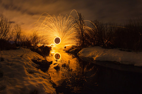 Abstract picture with trajectories of burning sparks on the surface creek at the background of spring night landscape