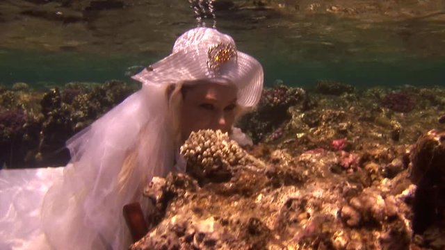 Model in white costume of pirate underwaterin Red Sea. Filming a movie. Young girl smiling at camera. Extreme sport in marine landscape, coral reefs, ocean inhabitants.