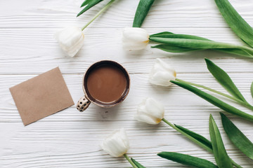 tulips with craft greeting card and coffee on white wooden rustic background with space for text. stylish flat lay with flowers and drink and empty paper. hello spring. modern instagram photo