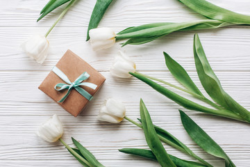 stylish craft present box and tulips on white wooden rustic background. flat lay with flowers and  space for text. hello spring. happy day concept. gift for celebration holiday