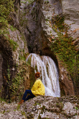 Chica joven de espaldas a la cámara mirando una cascada en una montaña 