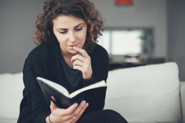 Young woman sitting on the sofa with open book and reading with interest. Soft focus image