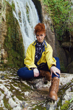 Chica joven y pelirroja posando frente a una cascada en una montaña 