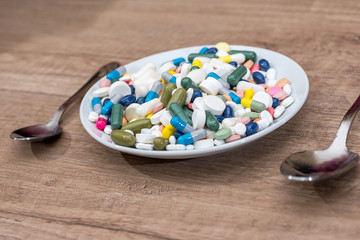 Colorful pills in plate with spoon on wooden background.