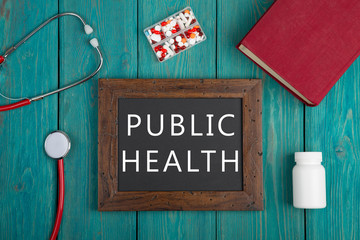 Blackboard with text "Public health", pills, book and stethoscope on wooden background