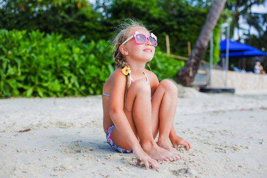 cute little girl in sunglasses and a swimsuit on the beach in paradise by the sea. Travel and Vacation. Freedom