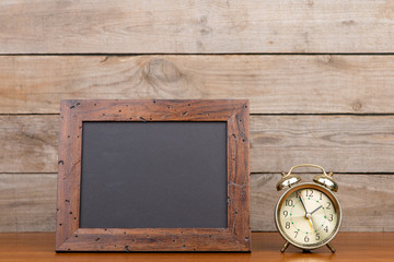 Alarm clock and blank blackboard on brown wooden background