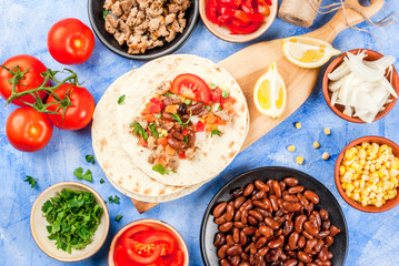 Cooking street fast Mexican food, freshly prepared, homemade sandwiches burrito with beans, beef, corn, peppers, tomatoes and herbs. On the blue background of concrete stone, close view copy space