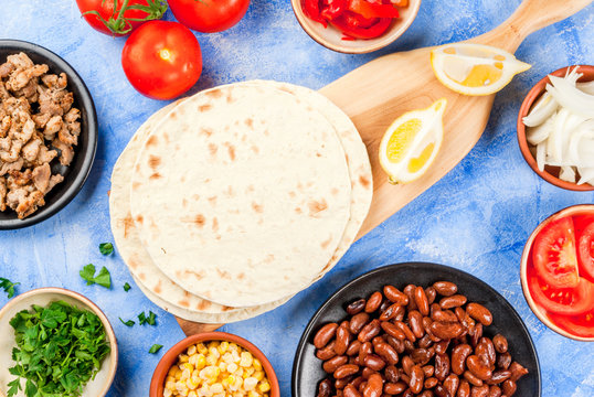 Cooking street fast Mexican food, freshly prepared, homemade sandwiches burrito with beans, beef, corn, peppers, tomatoes and herbs. On the blue background of concrete stone, close view copy space