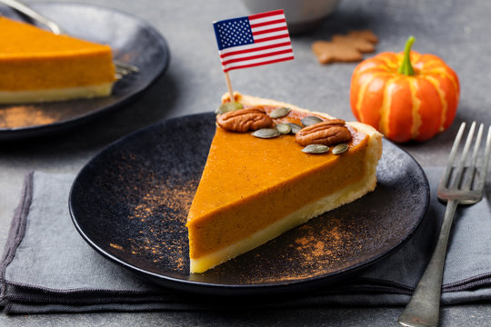 Pumpkin pie, tart made for Thanksgiving day on a black plate with American flag on top.