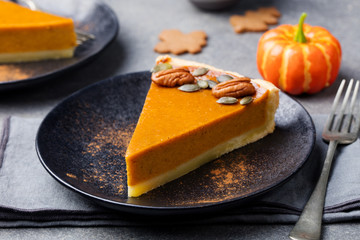 Pumpkin pie, tart made for Thanksgiving day on a black plate. Grey stone background.