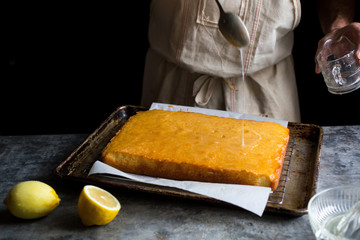 Person drizzling syrup onto lemon drizzle cake