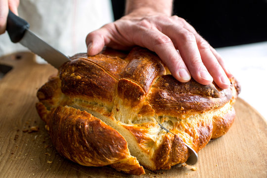 Man's hands cutting orange olive oil challah bread
