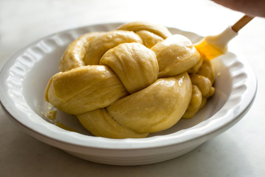 Person making orange olive oil challah bread, brushing dough with butter, close-up