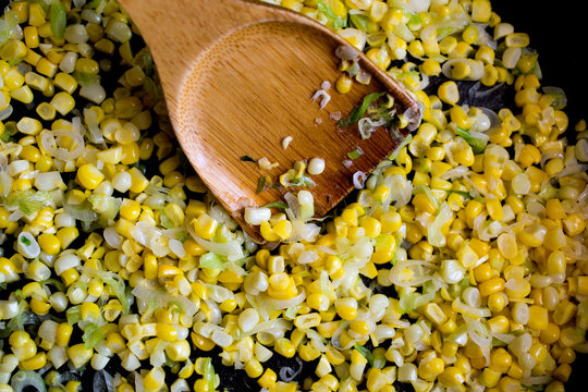 Sweetcorn in pan with sauce and wooden spoon, close-up