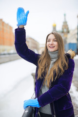 Beautiful girl with long hair in a warm jacket and waving to someone greets. She is dressed in a...
