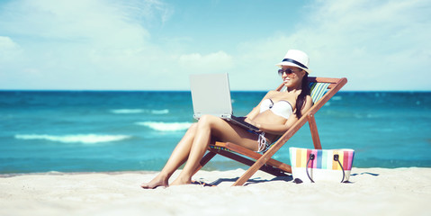 Young, beautiful, sporty and sexy woman with laptop relaxing on the beach. Traveling, vacation, concept.