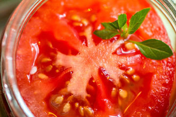 Canning fresh tomatoes with onions for winter in jelly marinade. Macro shot of basil leaves on top of a red ripe tomato slice being put in jar.