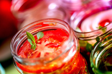Canning fresh tomatoes with onions for winter in jelly marinade. Macro shot of basil leaves on top of a red ripe tomato slice being put in jar.