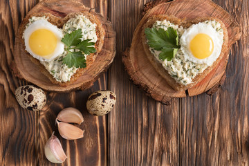 a sandwich in the shape of a heart with egg, cheese, dill, garlic on a wooden table