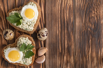 a sandwich in the shape of a heart with egg, cheese, dill, garlic on a wooden table