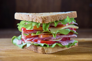 Sandwich with ham, cheese, tomatoes, lettuce, cucumbers and onions on a wooden background