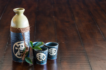 A bottle of sake and three sake cups on the rustic wood table.