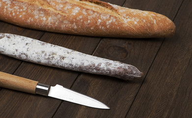 Bread fuet and a knife on wooden table. Spanish sausage. Horizontal shoot.