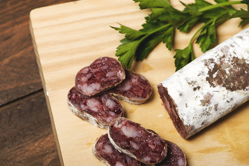 Close-up of cut fuet and a knife on a wooden board. Spanish sausage. Horizontal shoot.