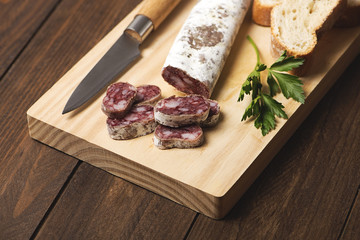 Fuet cut bread and knife on a wooden board. Spanish sausage. Horizontal shoot.