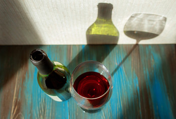 glass and bottle with red wine on wooden table in sunny day