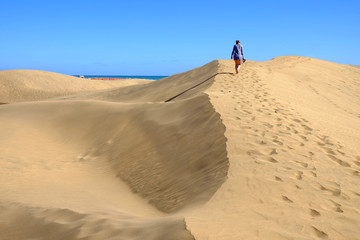 View on the dunes of Maspalomas and a young woman walking on them on the Canary Island Gran...