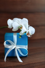 Gift and white orchid on a wooden background. The concept of celebration and a welcome card.