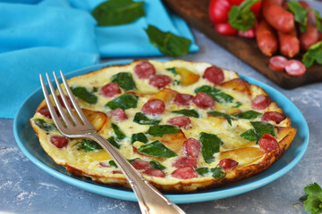 Omelet with spinach, cheese and Bavarian sausages on a concrete background