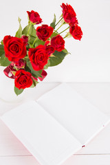 Bouquet of red roses with open notebook on white background