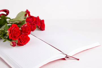 Bouquet of red roses with open notebook on white background