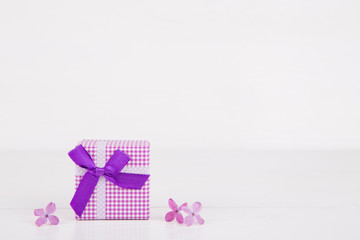 Purple gift box surrounded by lilac flowers on white background