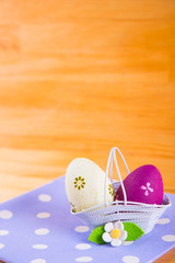 Colorful Easter eggs in basket with flower on fabric on wooden background