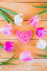 Bouquet of tender pink tulips with wicker heart on light wooden background